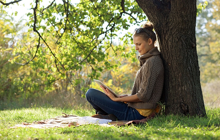 Distance education. Young woman sitting near from tree and worki